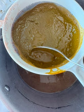 Spoon scooping thick brown liquid from a pot through a strainer.
